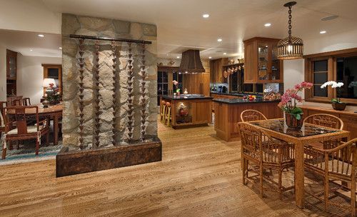 Spacious open-plan kitchen and dining area with wood cabinets, stone columns, and wicker table set