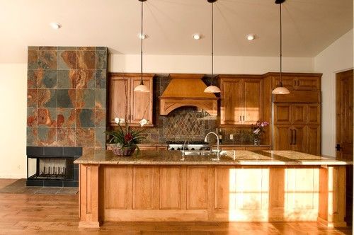 Spacious kitchen with wooden cabinets, island, granite counters, and a stone fireplace.