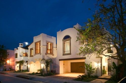 Luxury white stucco house at dusk with warm interior lights and a tree in the front yard