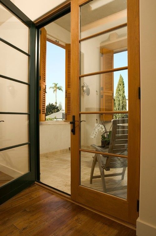 Open glass door to a sunlit patio with a chair and potted plants