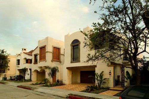 A yellow telehandler sits in front of a partially constructed house with green sheathing under a blue sky.
