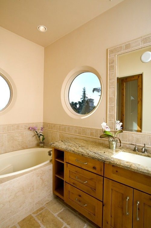Elegant bathroom with a corner tub, round window, wood vanity, and granite countertop
