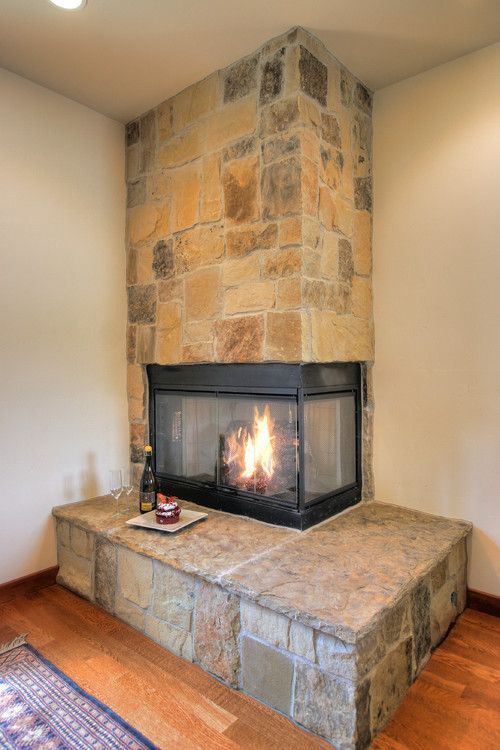 Stone corner fireplace with a lit fire and raised hearth in a room with wood floors