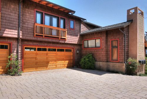 Modern brick home with wooden garage doors, balcony, and paved driveway