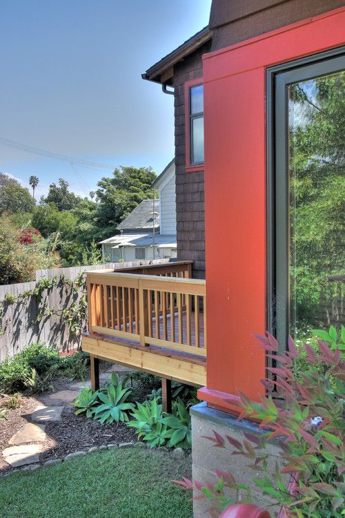 A wooden deck featuring a metal table with four chairs and a covered grill, overlooking a residential neighborhood.