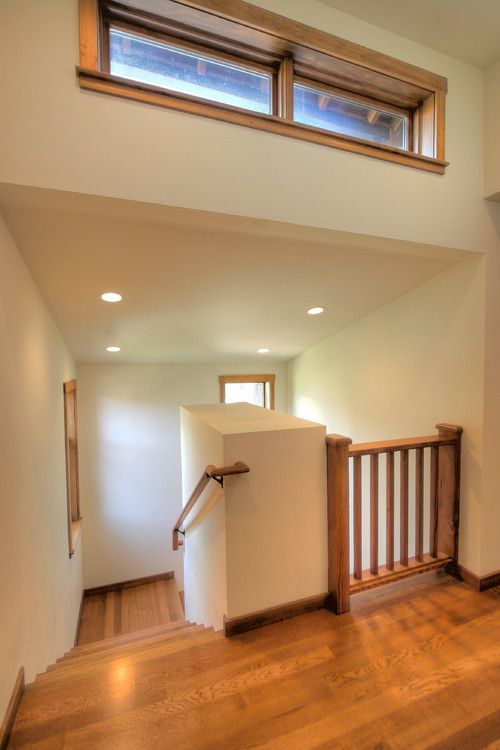 Bright hallway landing with wood floors, staircase railing, recessed lights, and high windows above.