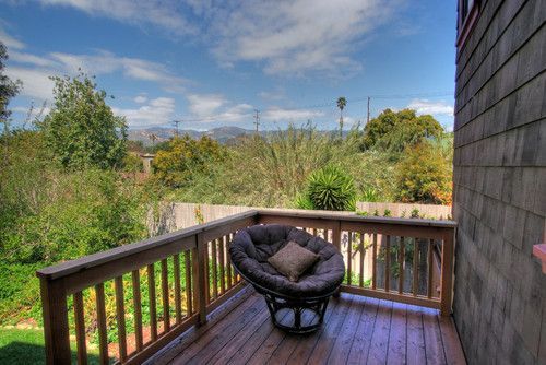 Wooden deck with cushioned chair overlooking a lush backyard and distant landscape under a blue sky