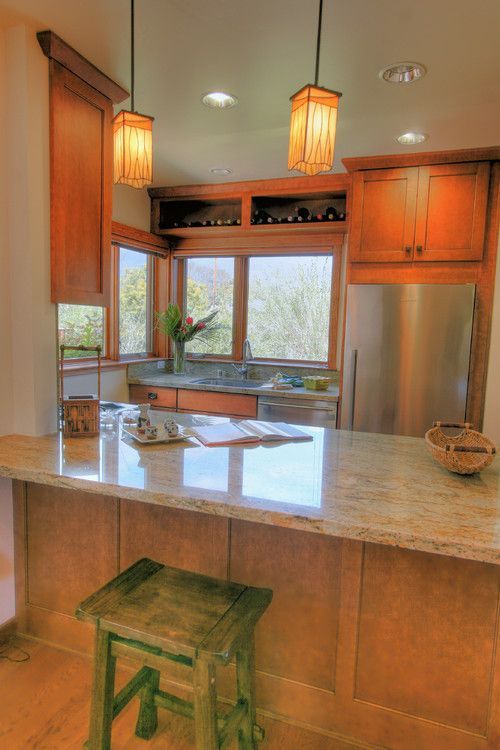 Warm wood kitchen with granite island, green stool, stainless fridge, and pendant lights by large windows