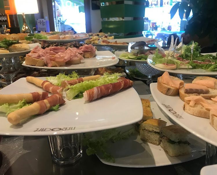 Vassoi di vari antipasti esposti in un bar; pane condito con carne, pesce e verdure.