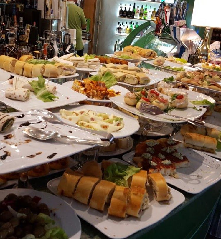 Tavolo da buffet imbandito con vari piatti; sullo sfondo una persona vestita di verde.