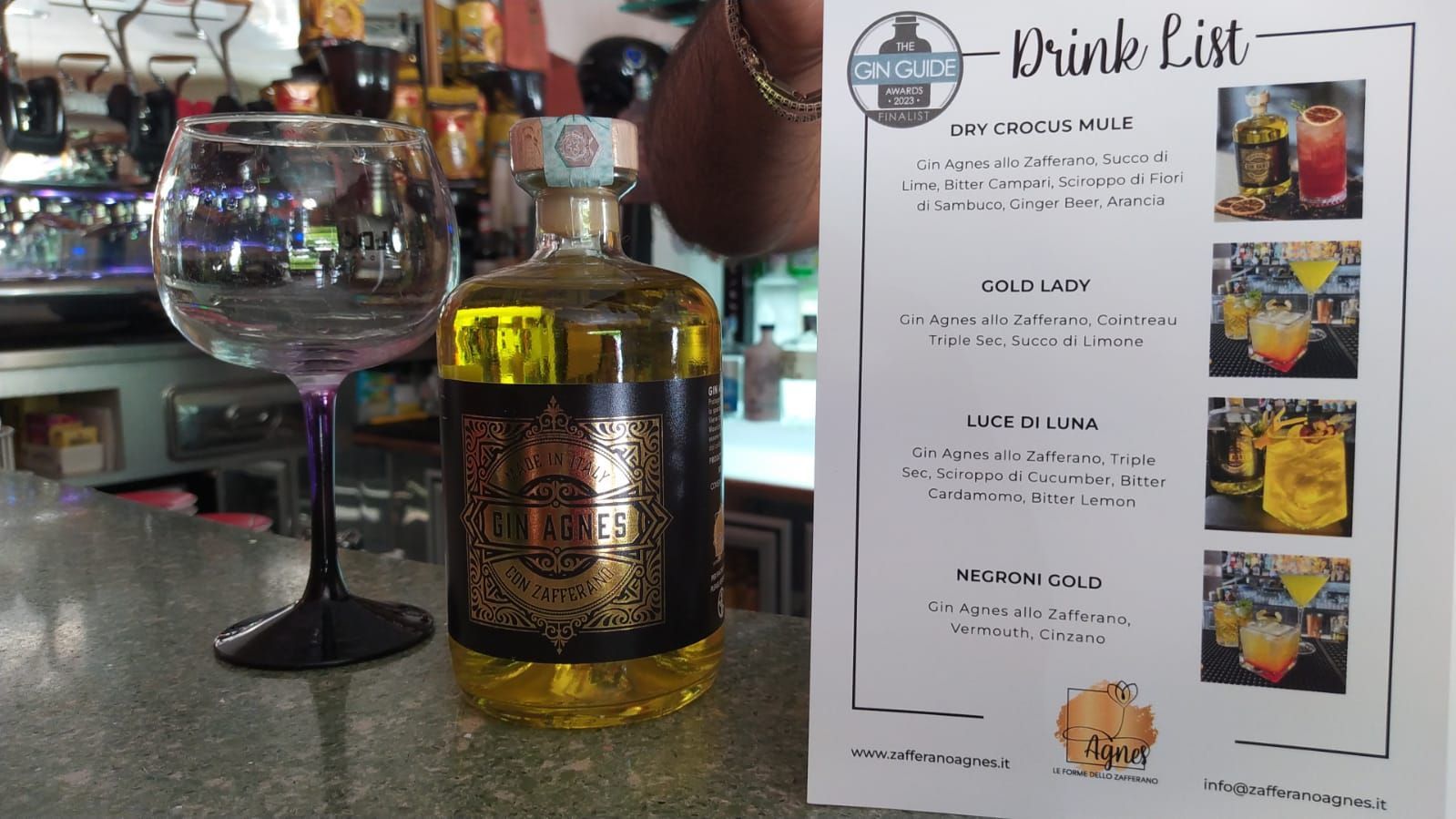 Una bottiglia di liquore giallo, un bicchiere e una lista di bevande su un bancone del bar.