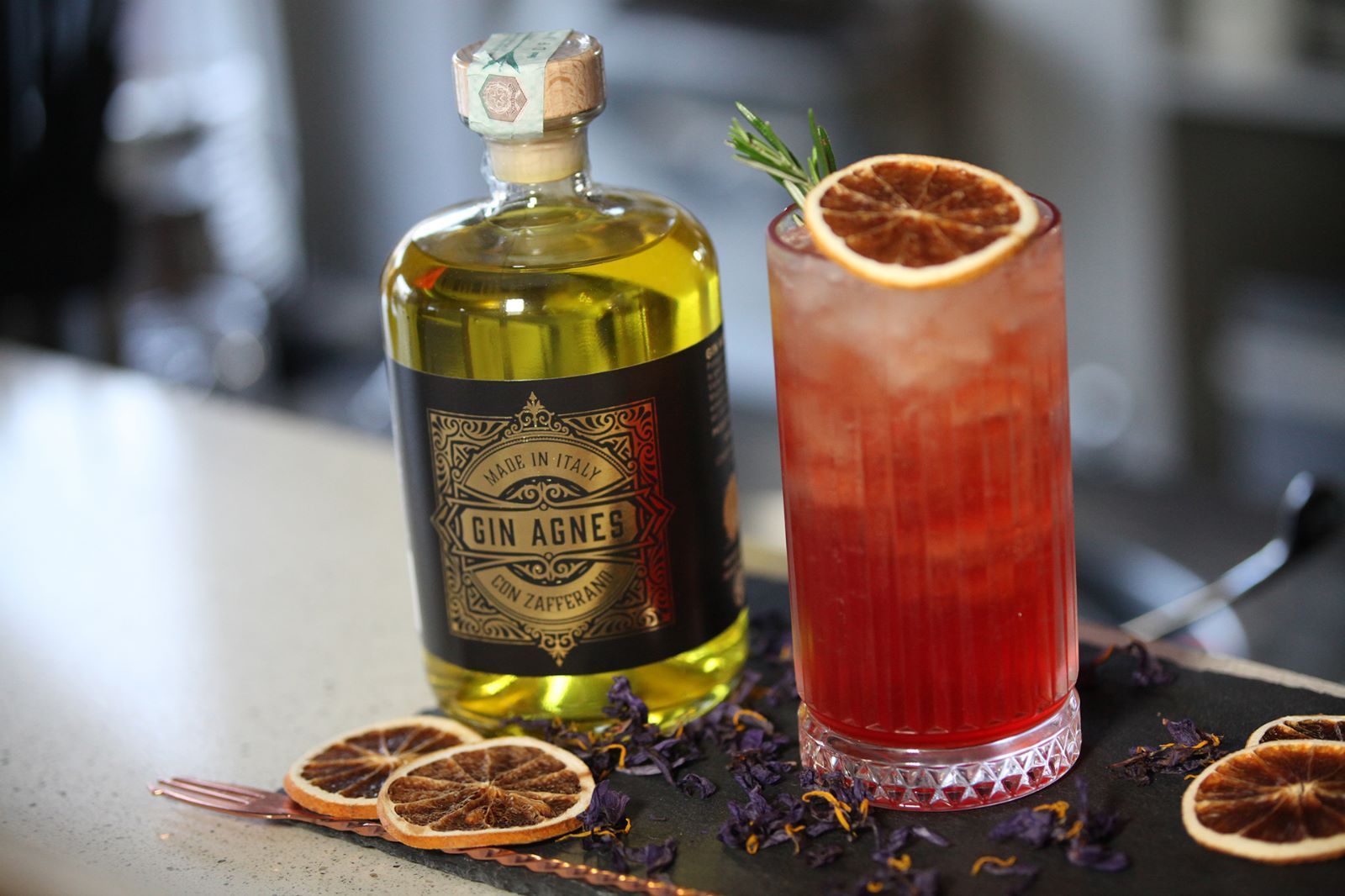 Bottiglia di liquore giallo e cocktail con guarnizione di fetta d'arancia su un bancone del bar.