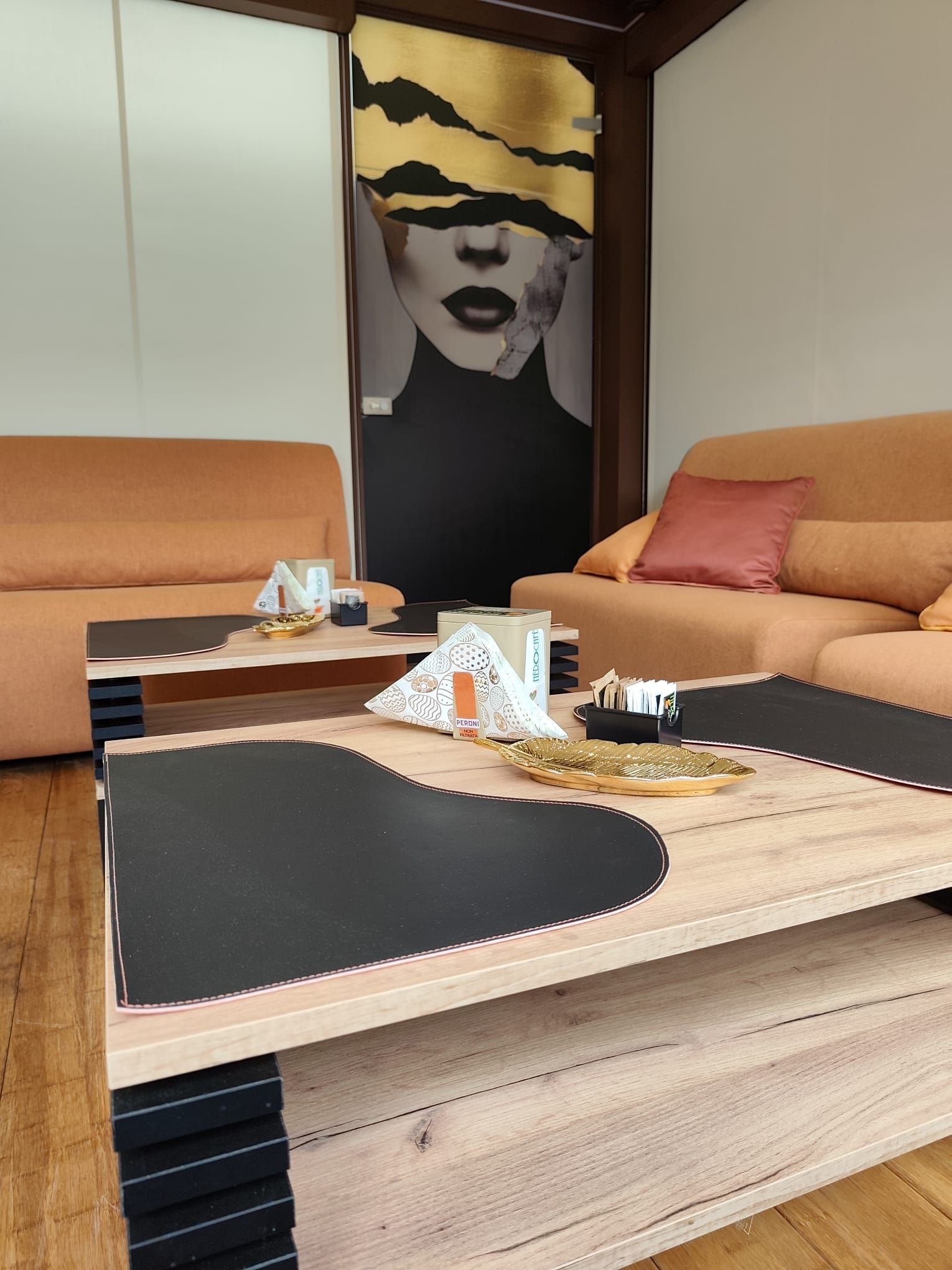 Soggiorno con divani arancioni, tavolini da caffè in legno e opere d'arte astratte raffiguranti una donna.