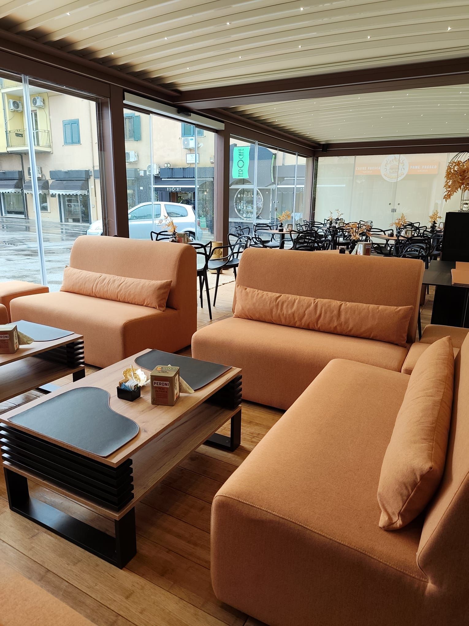 Tavolini e divani arancioni all'aperto, visibili attraverso le vetrate.