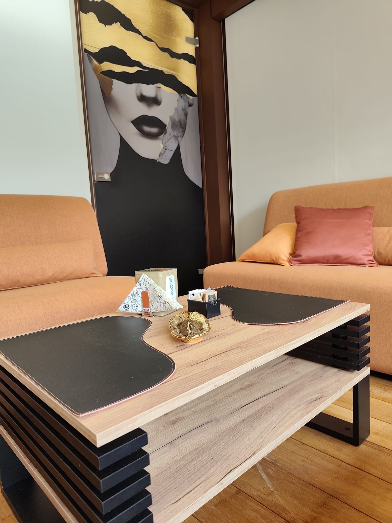 Tavolino da caffè con sezioni nere e beige, di fronte a un divano e a un'opera d'arte.