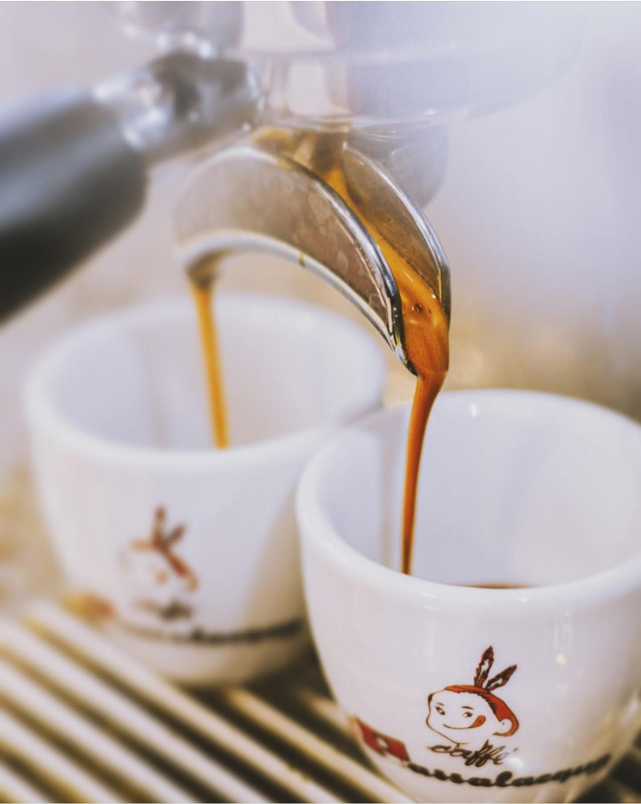 Macchina per caffè espresso che versa il caffè in due piccole tazze bianche.