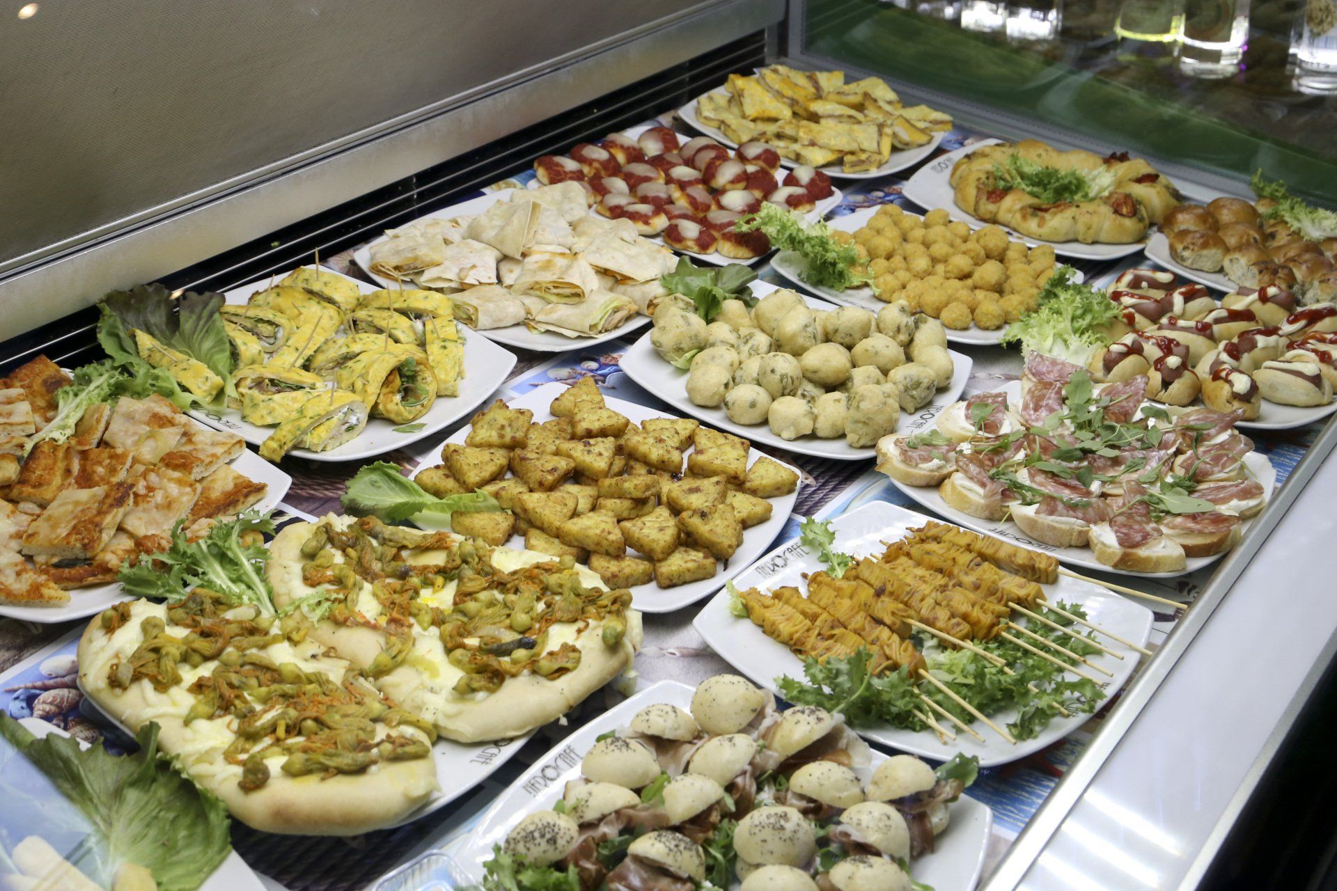 Assortimento di cibi preparati su piatti in una vetrina refrigerata; vari colori e consistenze.