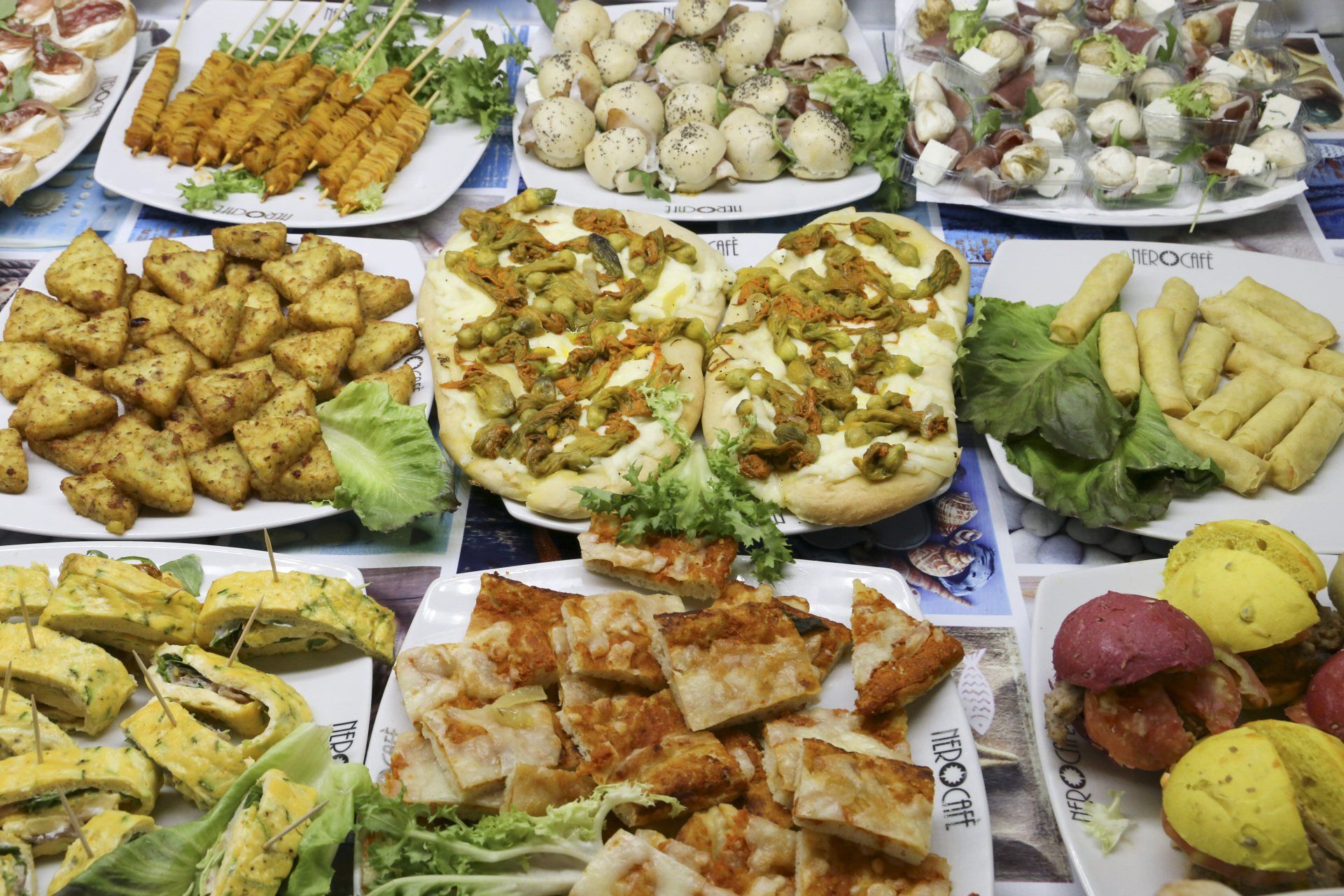 Assortimento di antipasti: fritti, focacce, panini ripieni e altri piccoli stuzzichini su piatti bianchi.