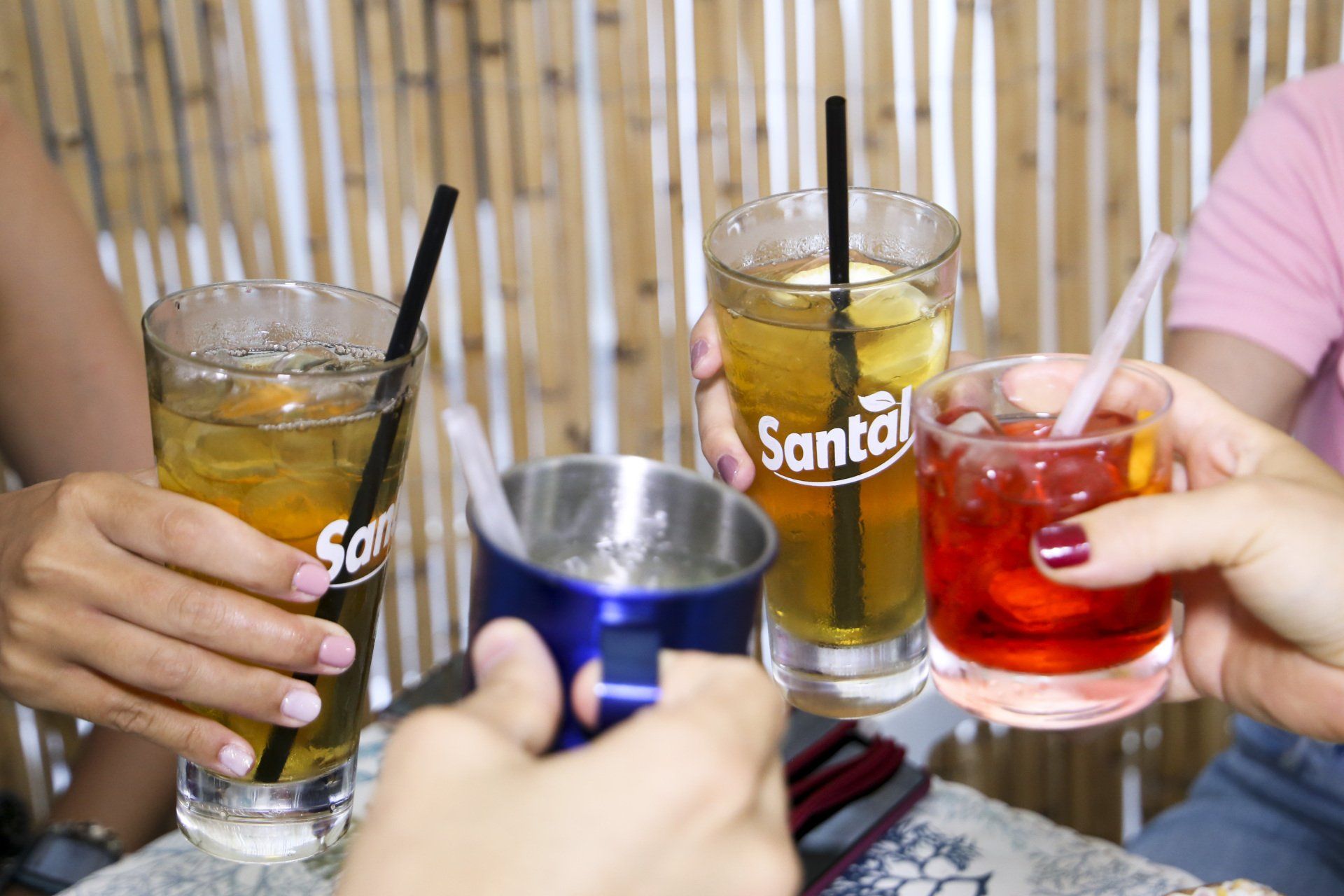 Quattro persone brindano a delle bevande: tè freddo, un cocktail rosso e un drink in una tazza di metallo blu.