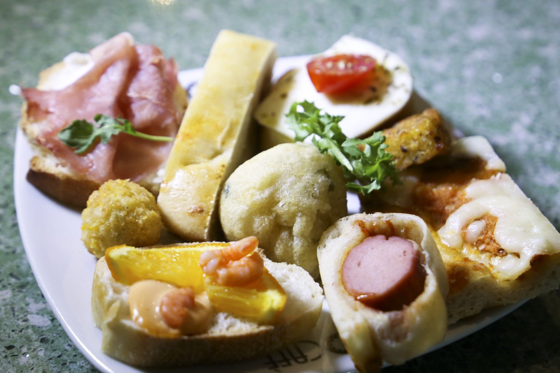 Piatto di vari antipasti, tra cui prosciutto su pane, pizza e polpette fritte.