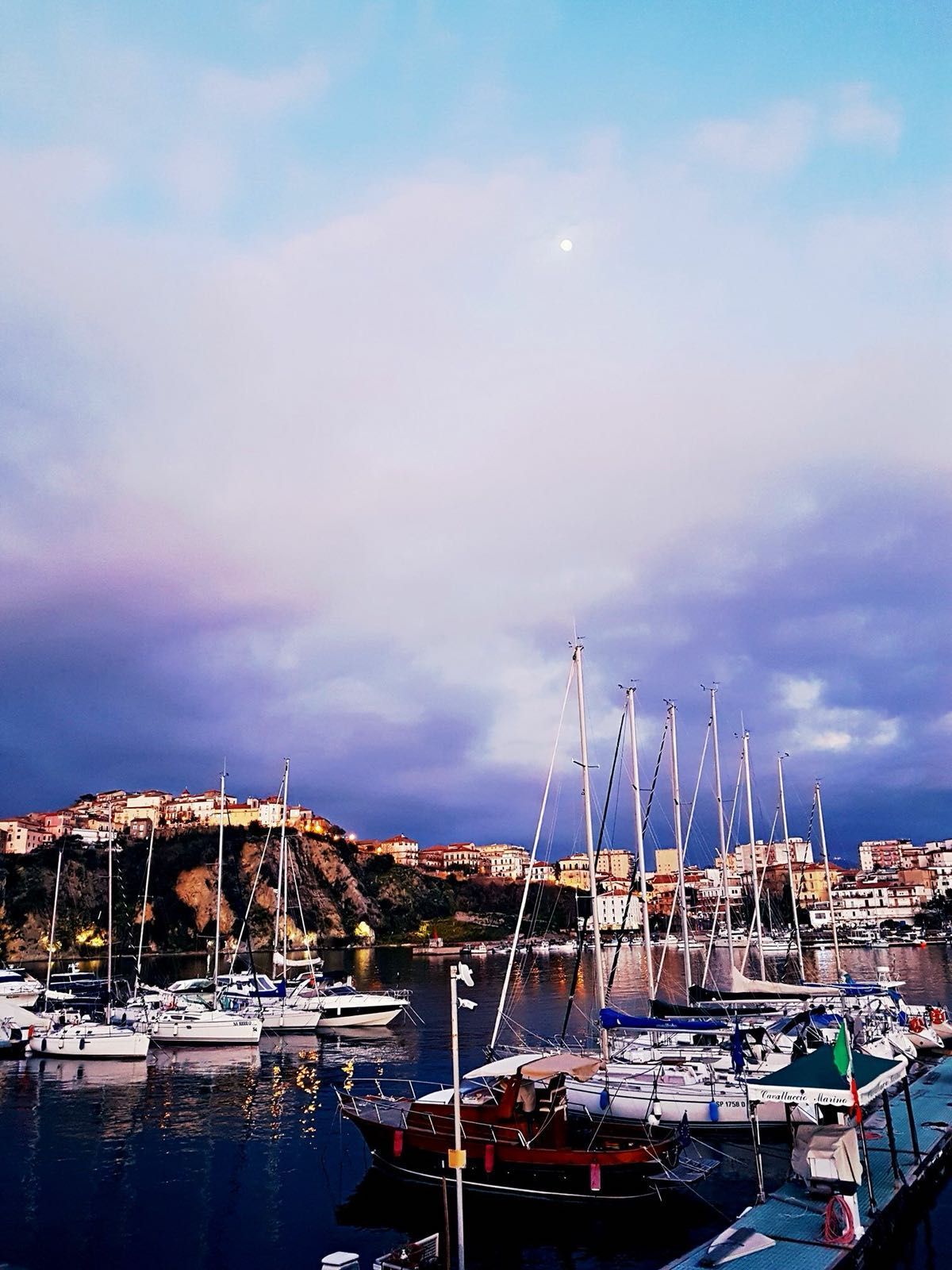 Barche attraccate nel porto sotto un cielo nuvoloso, edifici sulla scogliera.