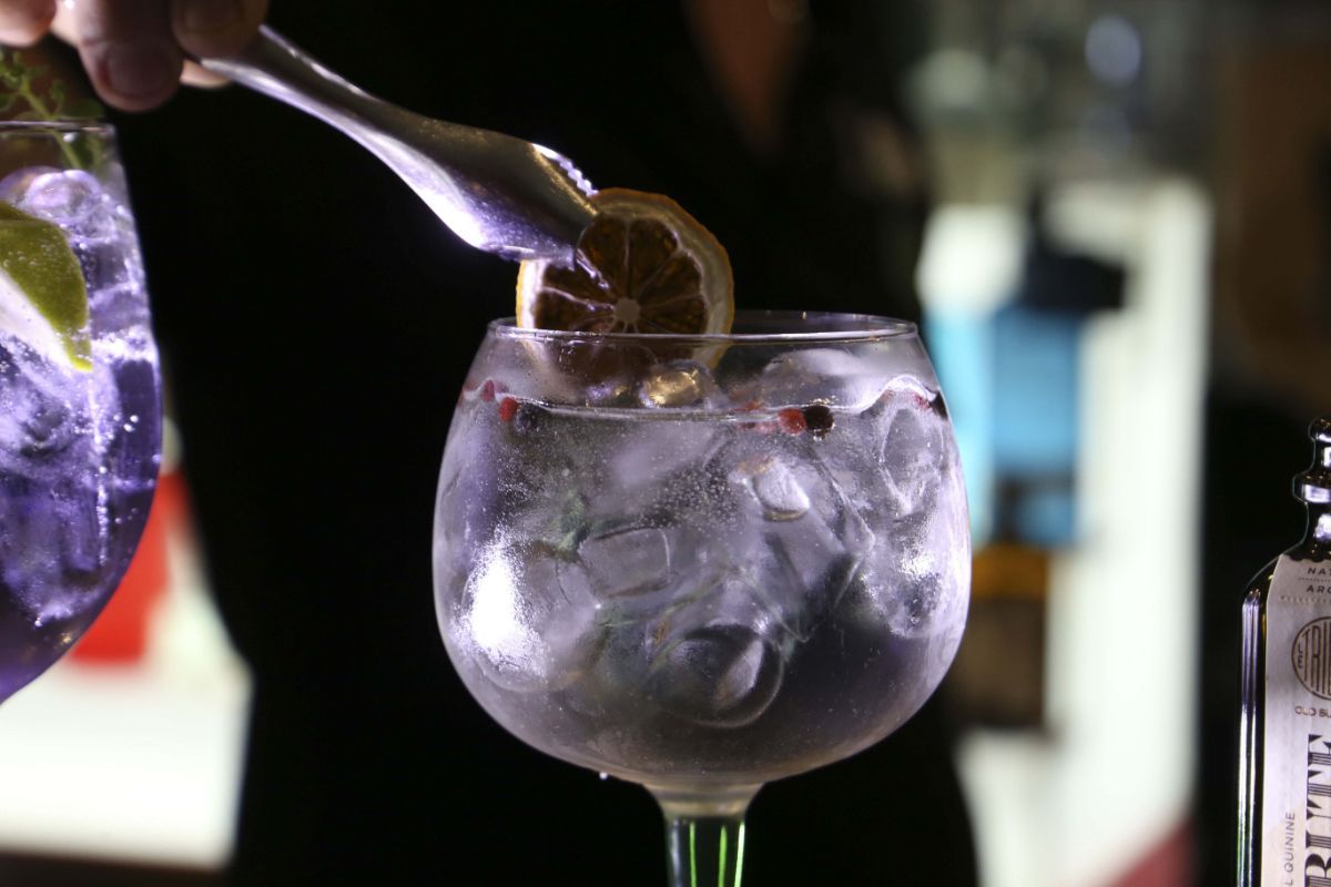 Barista che aggiunge una fetta di limone a un gin tonic con ghiaccio, in un bicchiere con stelo.