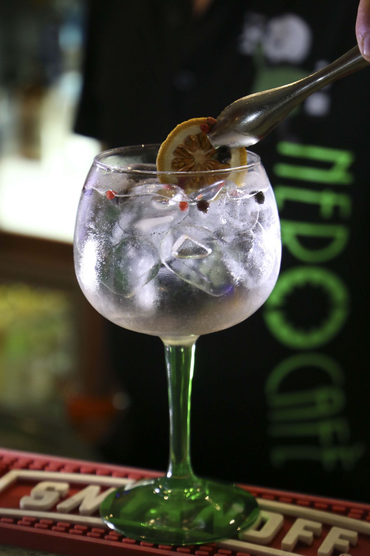 Cocktail gin tonic guarnito con una fetta di limone e grani di pepe, ambientazione da bar.