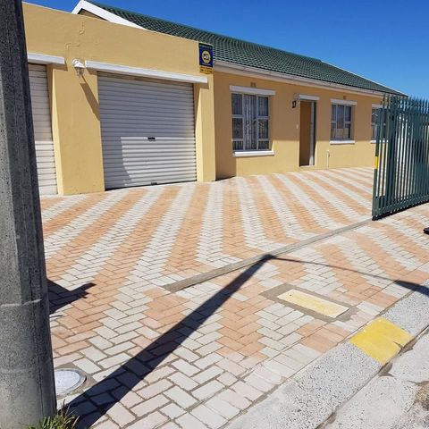 A yellow house with a green roof and a brick driveway