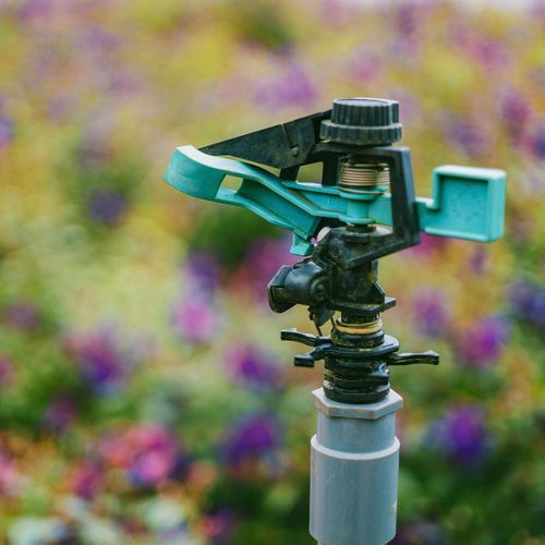 A green sprinkler is sitting in the middle of a field of flowers.