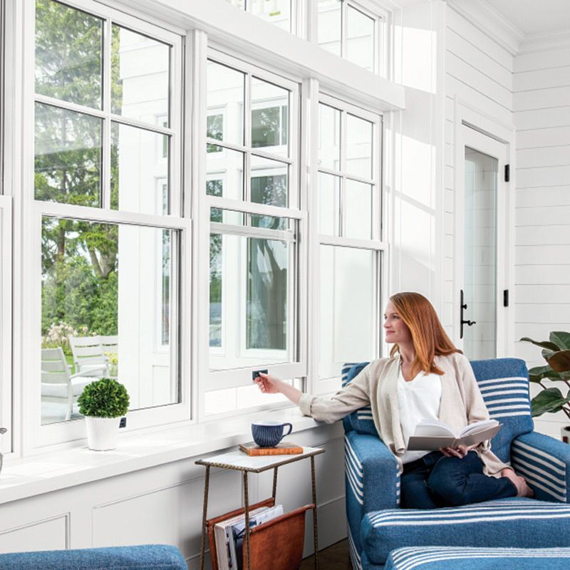 Woman on blue sofa adjusting window blind