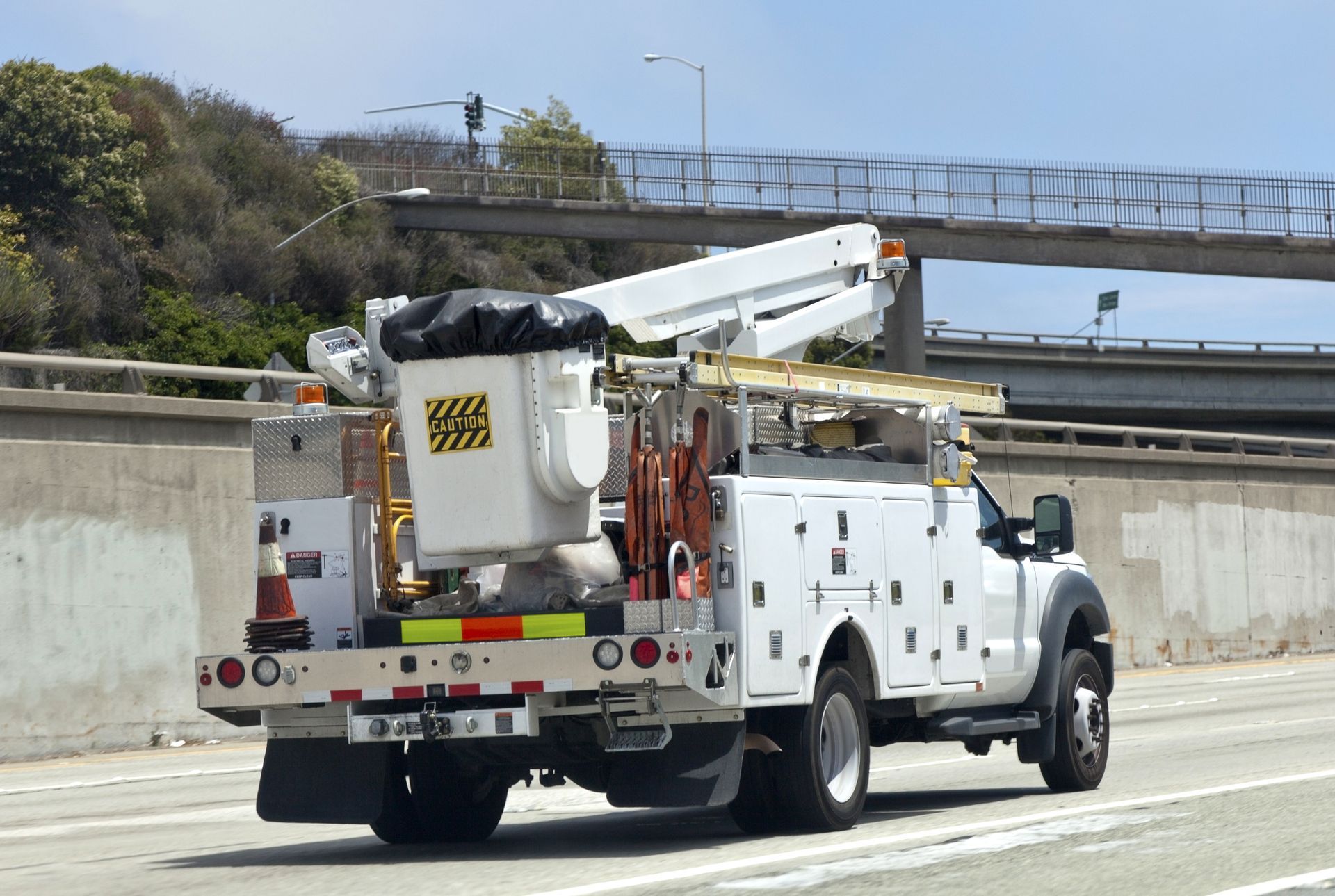 A white truck with a bucket on the back is driving down a highway.