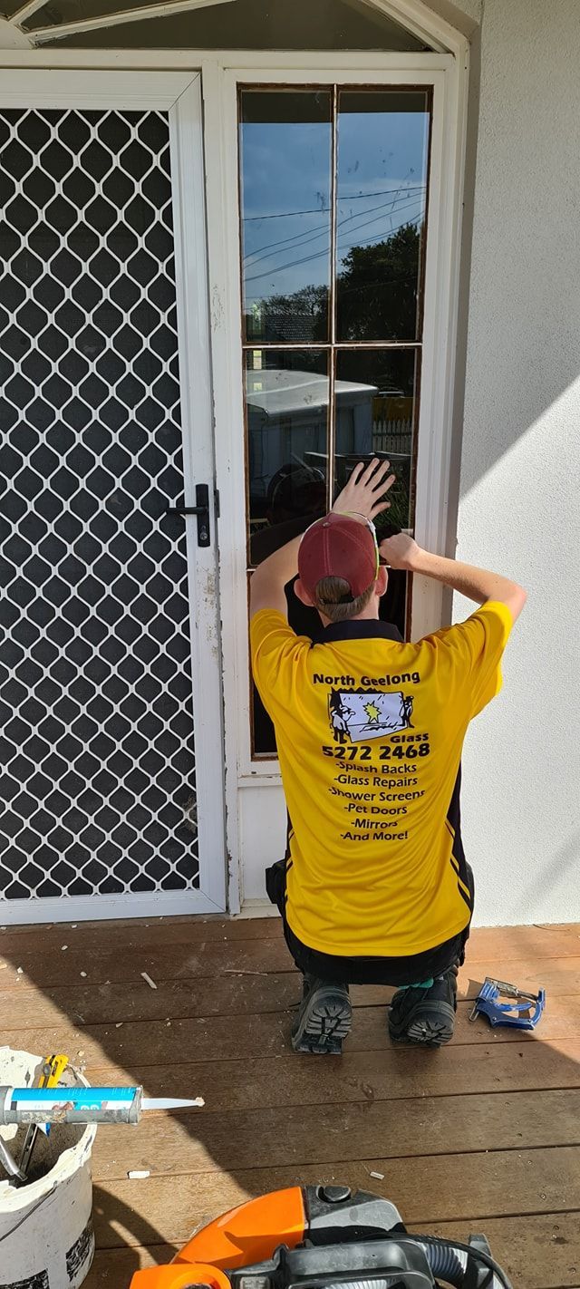 A man in a yellow shirt is installing a glass door.