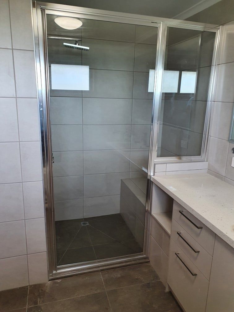 A bathroom with quality shower screen with aluminum a walk in shower and a sink.