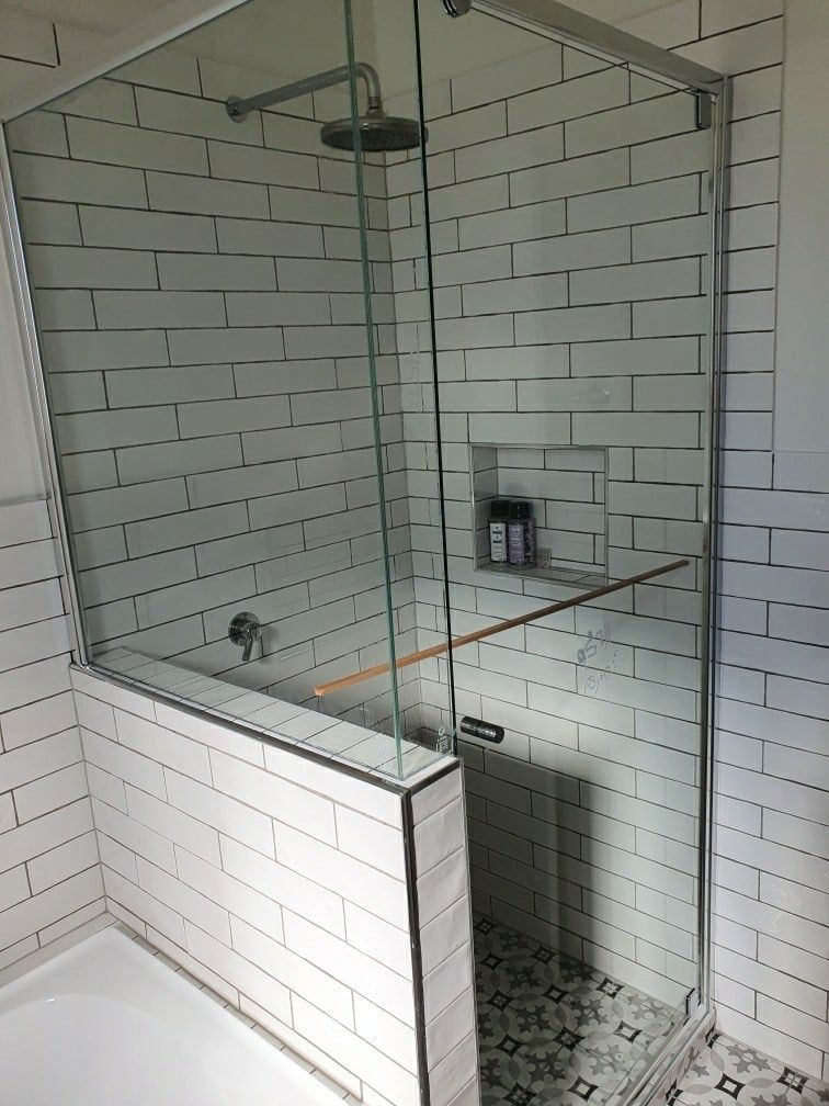 A bathroom with white tiles and a walk in shower with a glass door.