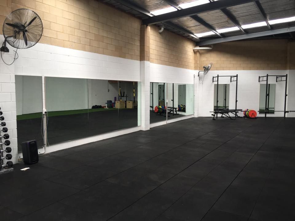 A gym with a lot of mirrors and a fan on the wall.
