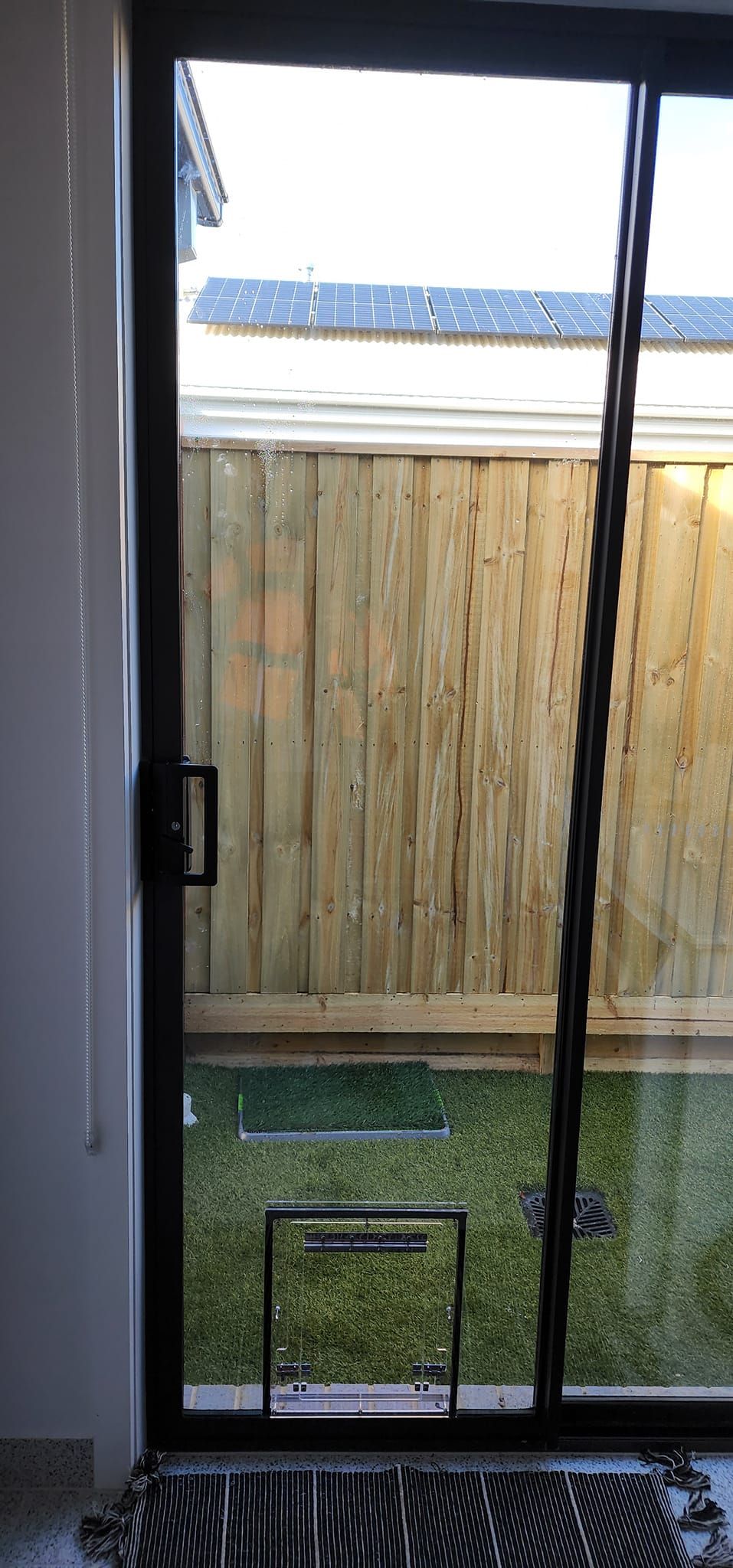 A sliding glass door is open to a backyard with a wooden fence.
