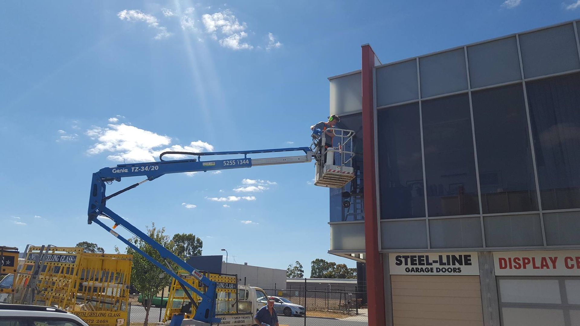 A man is standing on a crane in front of a building.
