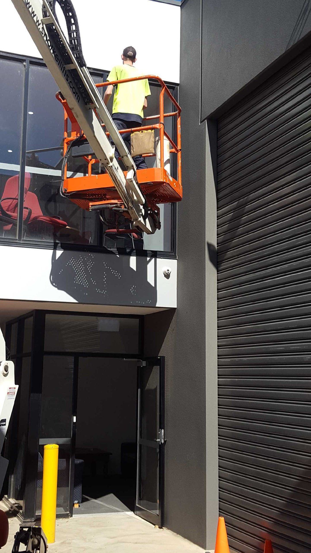 A man is standing on a lift estimating in front of a building.