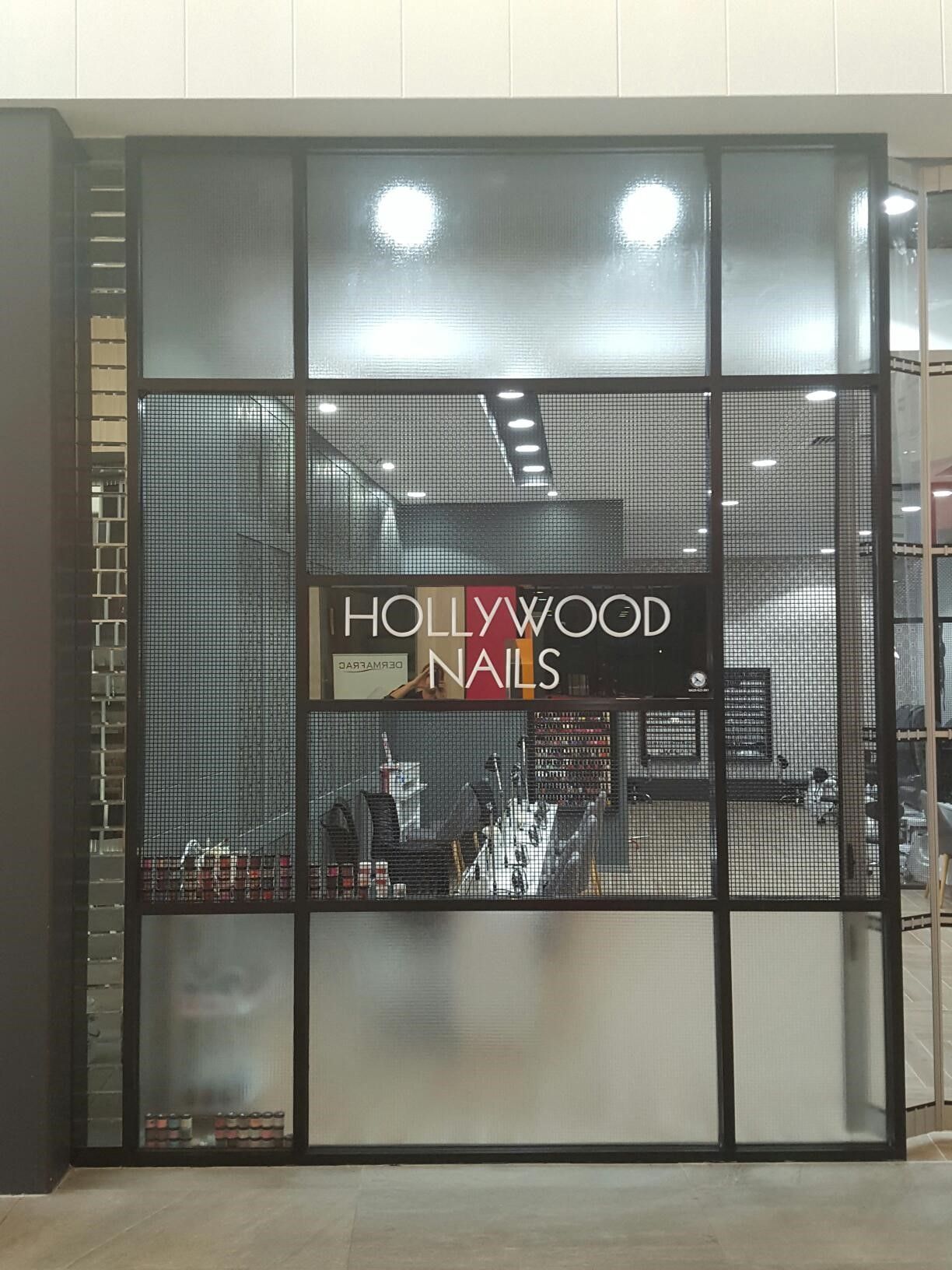 Hollywood Nails storefront with black-framed windows, frosted glass, and a wire mesh. Interior visible with tools.