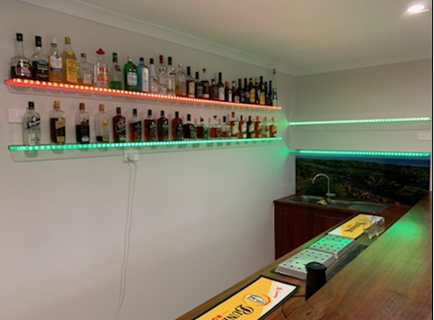 Home bar with liquor bottles on lit shelves. Green and orange LED lights illuminate the bottles.