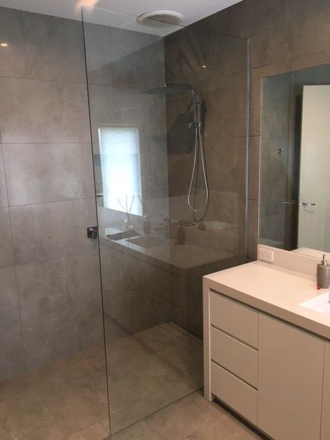 Bathroom with a glass shower, white vanity, and gray walls and floor.