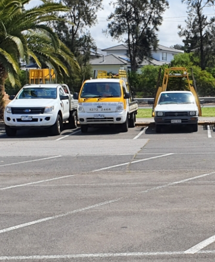 Three vehicles parked in a lot, a white pickup truck, a yellow truck, and a white car.