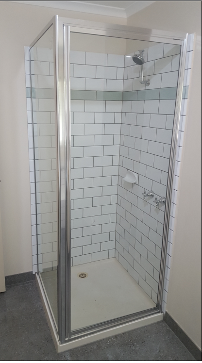 Shower stall with glass doors, white brick-like tile walls, chrome fixtures, and a white base.