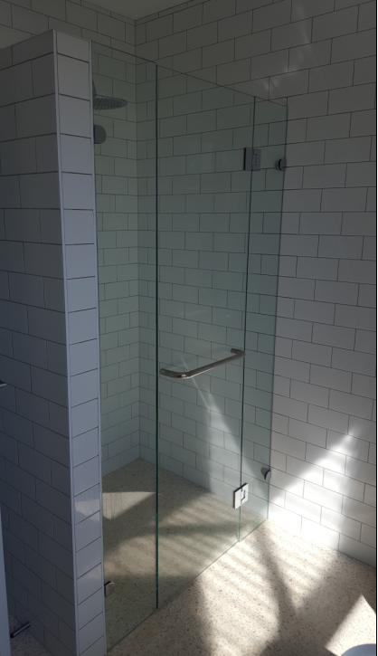 Glass shower enclosure with white subway tile walls and a silver handle.