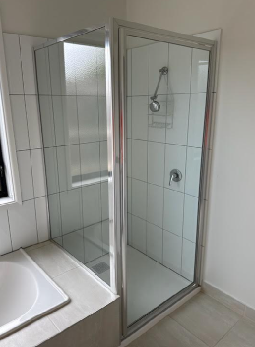 Shower enclosure with a glass door, on white tiled walls, in a modern bathroom.