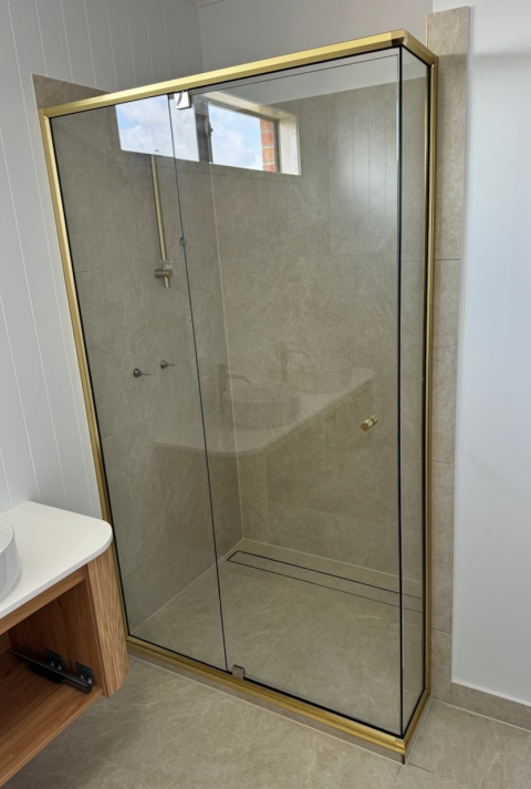 Shower stall with gold trim and glass doors.