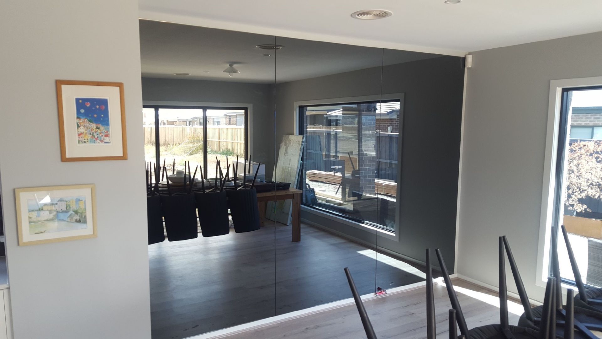 Interior view of a room with grey walls, large windows, and chairs stacked against a table.