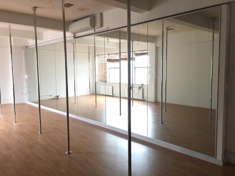 Empty dance studio with mirrors, poles, and wood floors.