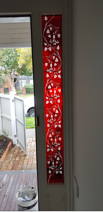 A red stained-glass window panel with white floral design next to an open door.