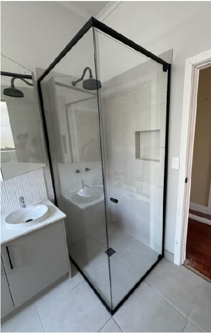 Bathroom with a black-framed glass shower stall, white sink, and light gray vanity.